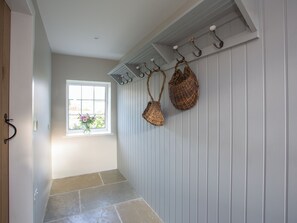 A hallway with a window, a coat rack with woven baskets, and a tiled floor.