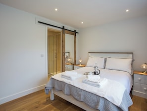 A bedroom with a bed, bedside tables, a nightstand, a mirror, a shower area, and a wooden floor.