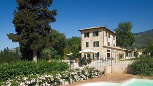 Un bâtiment à deux étages doté d’une piscine, entouré d’une végétation luxuriante et surplombé d’un ciel d’un bleu éclatant.