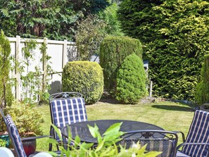 A garden with a white fence, a neatly trimmed hedge, and a metal table with chairs.