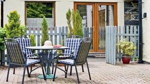 Une terrasse avec une table ronde et quatre chaises, une petite plante en pot et une clôture en bois.