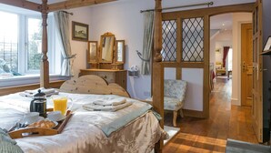 Un dormitorio con cama con dosel, un armario de madera, una silla y vistas al exterior a través de una ventana.