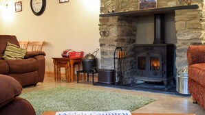 A cozy living room with a stone fireplace, a brown leather sofa, a wooden table, and a green rug. - 3 bedroom accommodation in Llangeitho, near Tregaron (Llangeitho, near Tregaron)