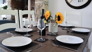 Une table à manger dressée avec des assiettes, des couverts et des verres à vin, avec un mur en pierre et un grand miroir rond en arrière-plan.