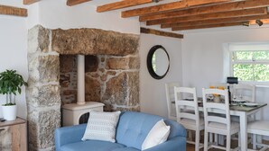 Un salon chaleureux avec une cheminée en pierre, un canapé bleu et un coin repas avec des chaises blanches et une table mise pour deux personnes.