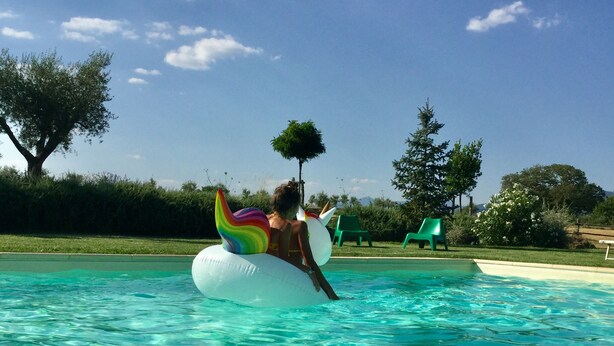 Una persona flota sobre un unicorn de colors inflable en una piscina de blau translúcid.