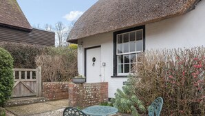 A quaint cottage with a thatched roof, a white door, and a small garden with a table and chairs. - 1 bedroom accommodation in Nether Wallop, near Stockbridge (Nether Wallop, near Stockbridge)