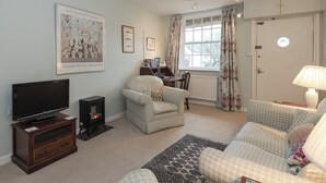 A living room with a television, a fireplace, a sofa, a chair, and a window with curtains. - 1 bedroom accommodation in Nether Wallop, near Stockbridge (Nether Wallop, near Stockbridge)