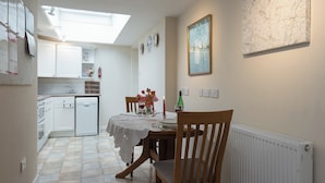 A compact kitchen with white cabinets, a small fridge, and a dining area with a table set for two. - 1 bedroom accommodation in Nether Wallop, near Stockbridge (Nether Wallop, near Stockbridge)