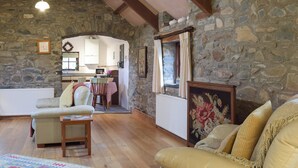 Uma sala de estar acolhedora com parede de pedra, vigas de madeira, espaço de jantar com mesa e cadeiras e lareira.