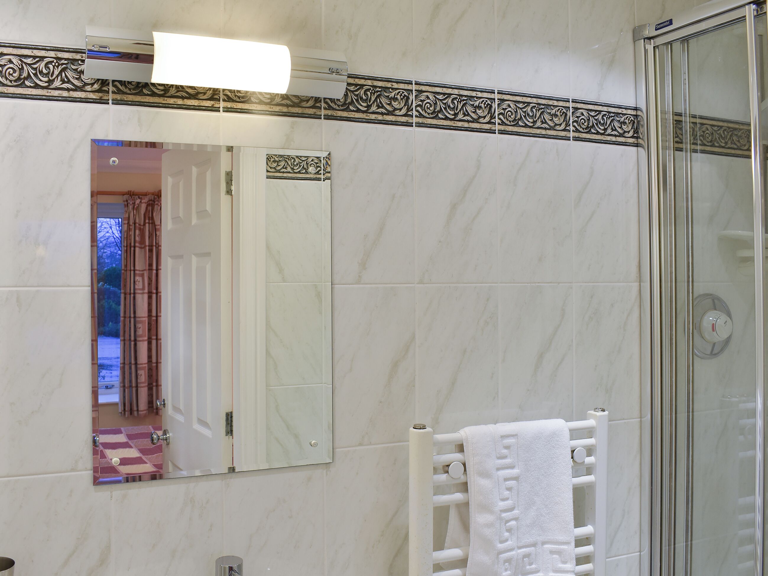 Une salle de bain avec une douche, un porte-serviettes et un miroir.