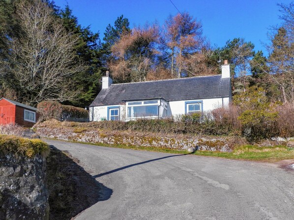 A rural house with a sloped roof, a chimney, and a small adjacent shed. - 2 bedroom accommodation in Helmsdale, near Brora (Helmsdale, near Brora)