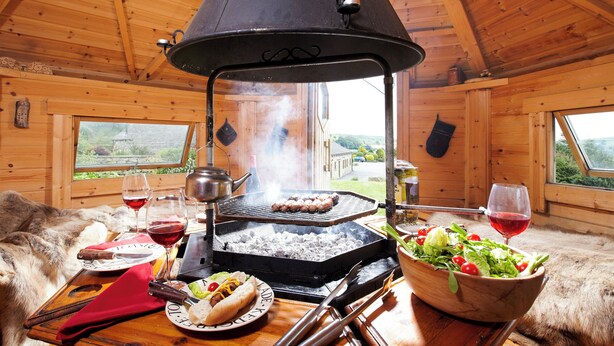 Un intérieur en bois avec un barbecue, un saladier rempli de salade et un canapé recouvert de fourrure.