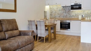 Une cuisine moderne avec des armoires blanches, un four encastré et un four à micro-ondes. On y trouve également un coin repas avec une table en bois et des chaises à carreaux.