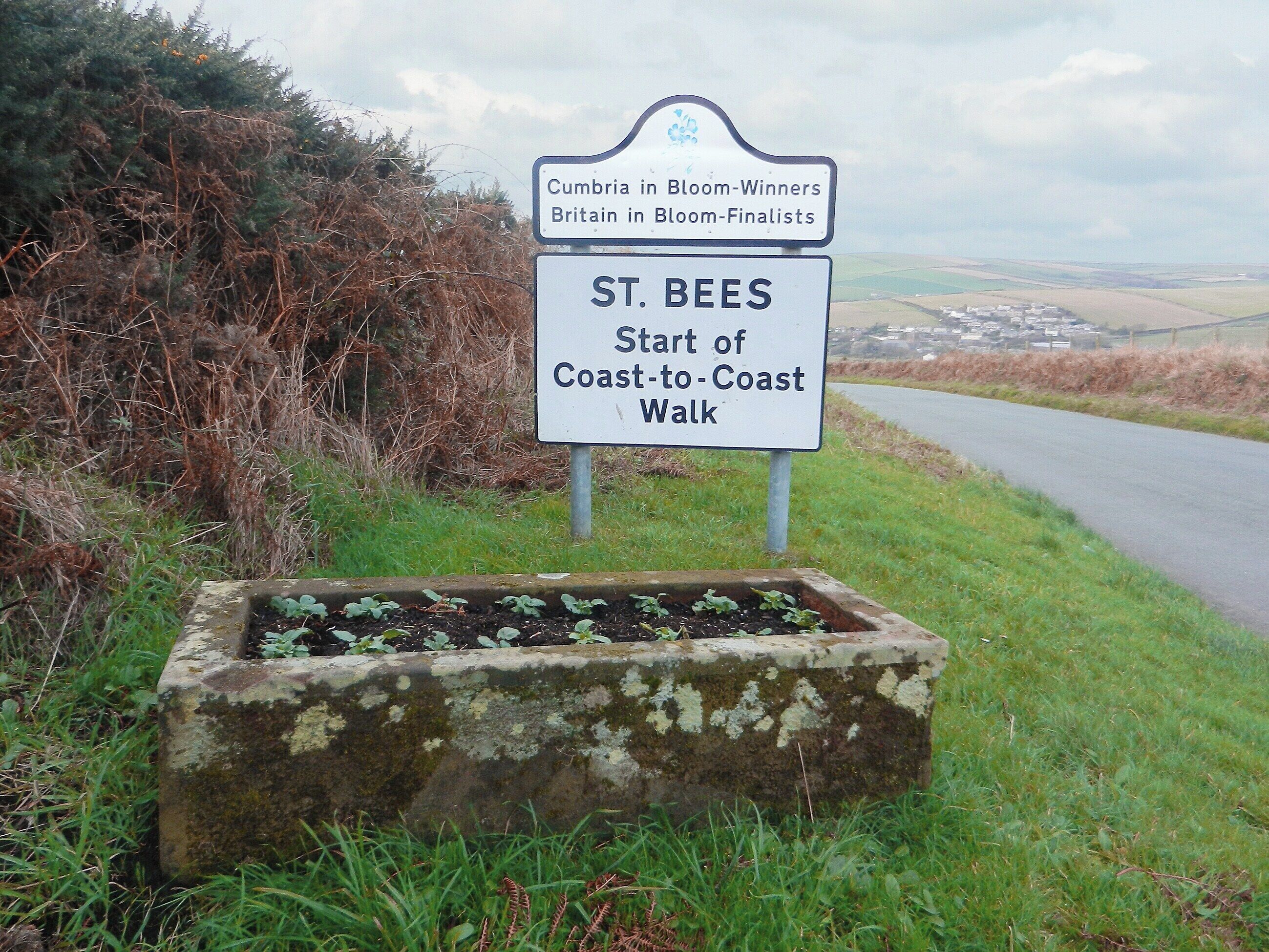 Une pancarte indique que Cumbria a remporté un prix pour ses aménagements floraux et qu’elle a été sélectionnée comme finaliste dans un concours national britannique. Elle marque également le point de départ de la randonnée « Coast-to-Coast Walk » à St. Bees.