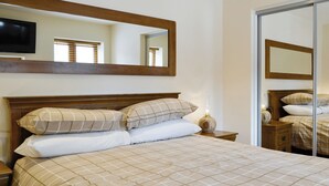 Un lit bien fait, avec une couvre-lit à carreaux, une tête de lit en bois et une lampe de chevet.