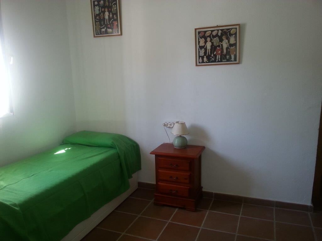 Una habitación pequeña y sencilla con una cama individual, una mesita de noche de madera con una lámpara y dos cuadros en la pared.