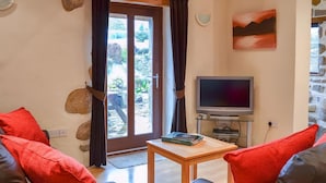 Una sala de estar con un sofá, una mesa de centro, una televisión y una pared de piedra.