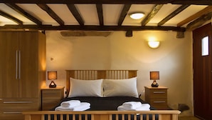 Un dormitorio con una cama de madera, dos mesitas de noche con lámparas, un armario y un techo inclinado con vigas a la vista.