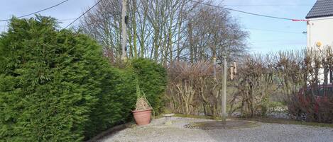 A gravel driveway leading to a building with a tiled roof, surrounded by trees and a large evergreen bush.