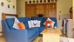 Ein Wohnzimmer mit einem blauen Sofa, einem Holztisch und einer dahinterliegenden Küchenzeile.