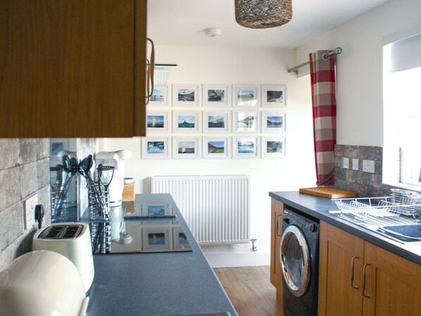 A modern kitchen with a built-in washing machine, a countertop with a dish rack, and a wall of framed pictures. - 1 bedroom accommodation in Wiggonby, near Carlisle (Wiggonby, near Carlisle)