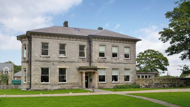 A two-story stone building with a symmetrical facade, large windows, and a central entrance.