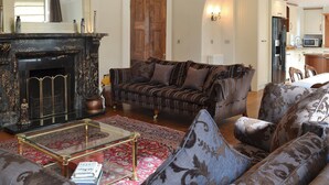 A living room with a fireplace, a sofa set, a coffee table, and a kitchen in the background.