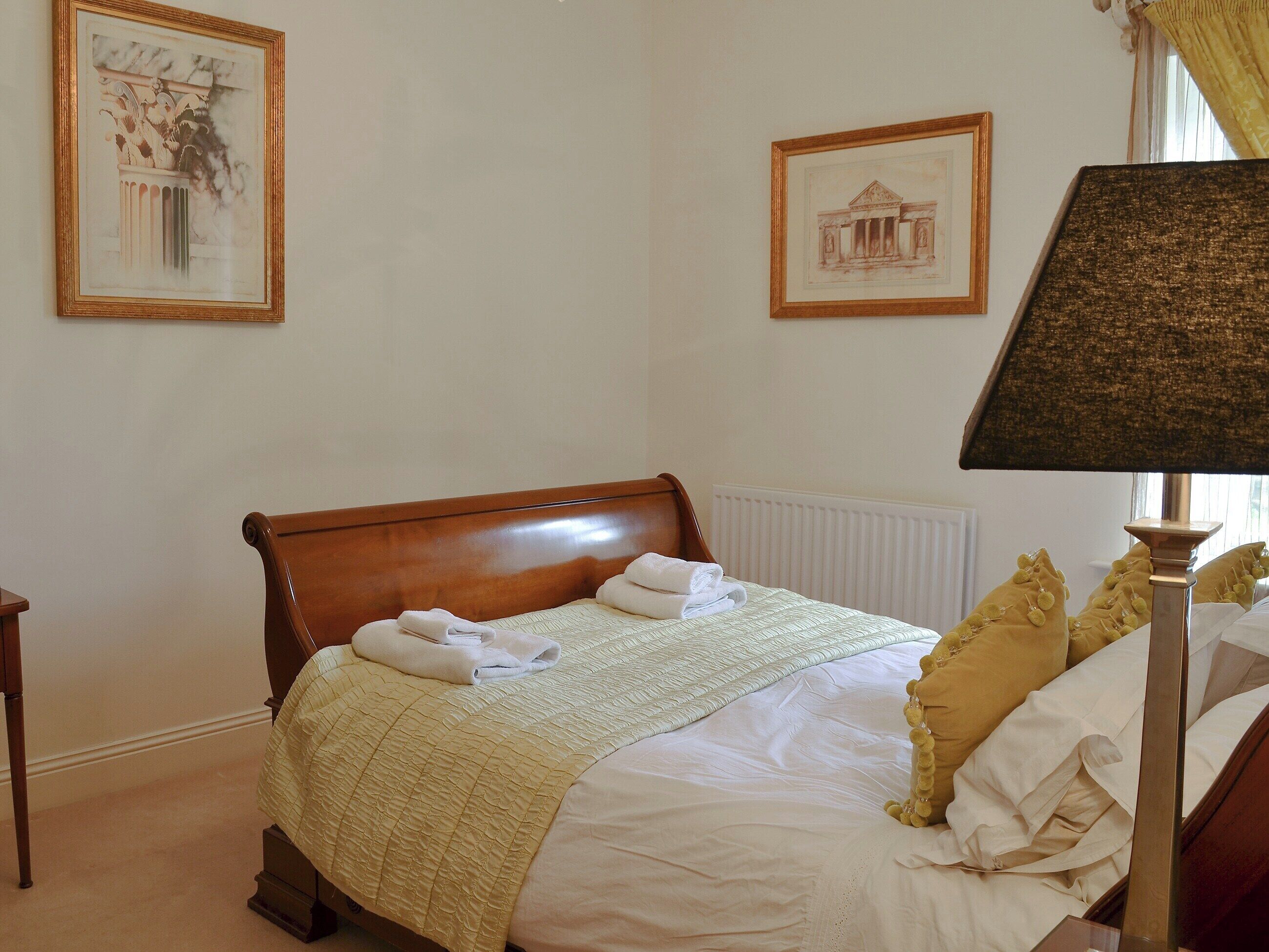 A neatly made bed with a headboard, a bedside lamp, and two framed pictures on the wall.