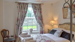 A bedroom with a bed, a chair, a window with curtains, and a lamp.