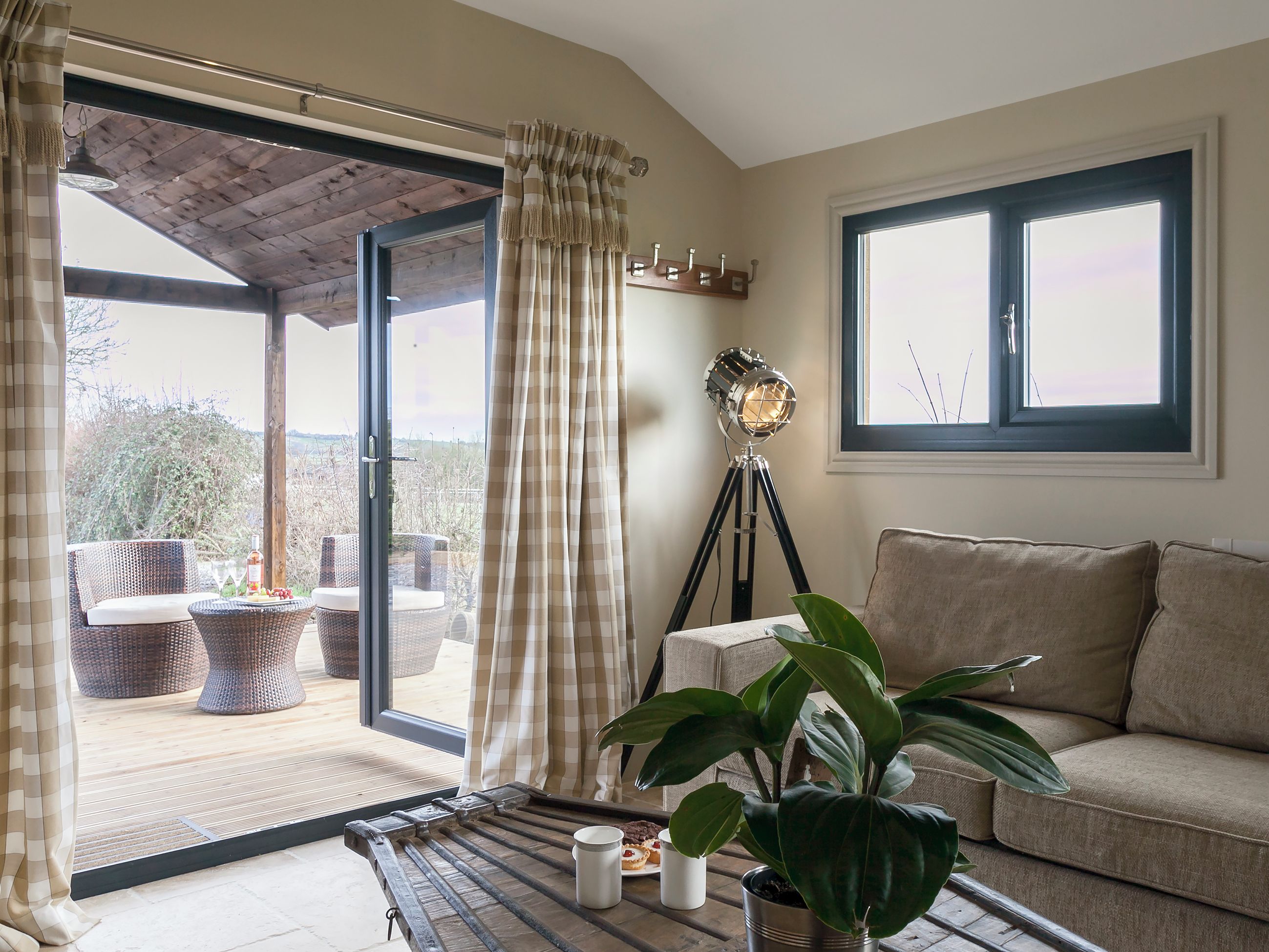 A room with a sliding glass door leading to an outdoor seating area, a floor lamp, a sofa, and a potted plant.