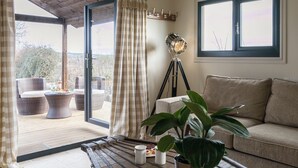 A room with a sliding glass door leading to an outdoor seating area, a floor lamp, a sofa, and a potted plant. - 1 bedroom accommodation in Rudford, near Gloucester (Rudford, near Gloucester)