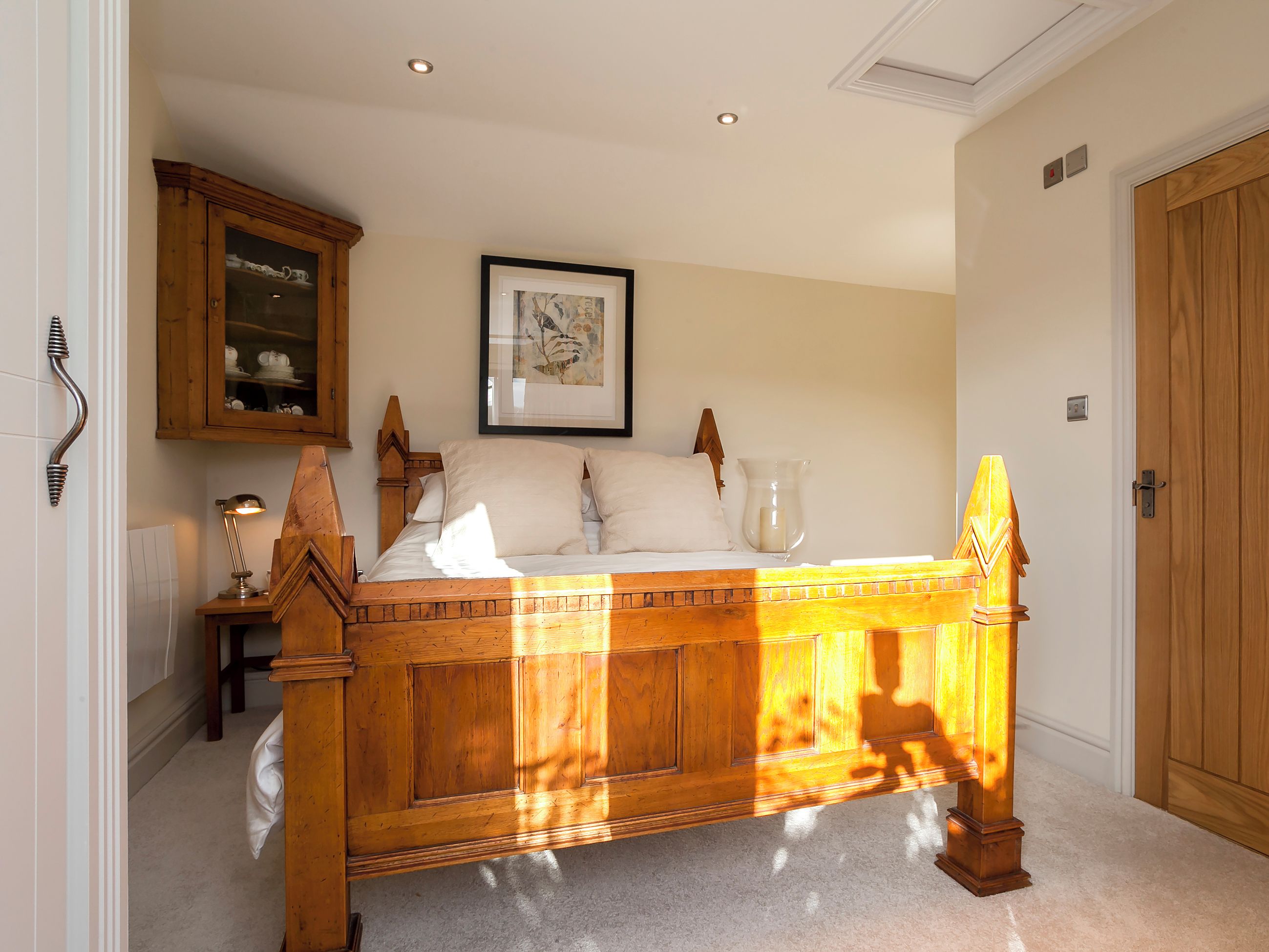A bedroom with a wooden bed, a framed picture on the wall, and a cabinet above the bed.