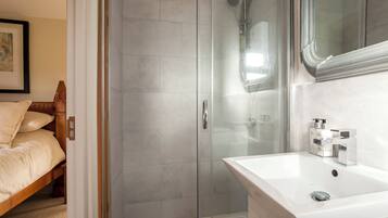 Un baño moderno con ducha envuelta en vidrio, un lavamanos blanco con espejo y una cama de madera en la habitación contigua.