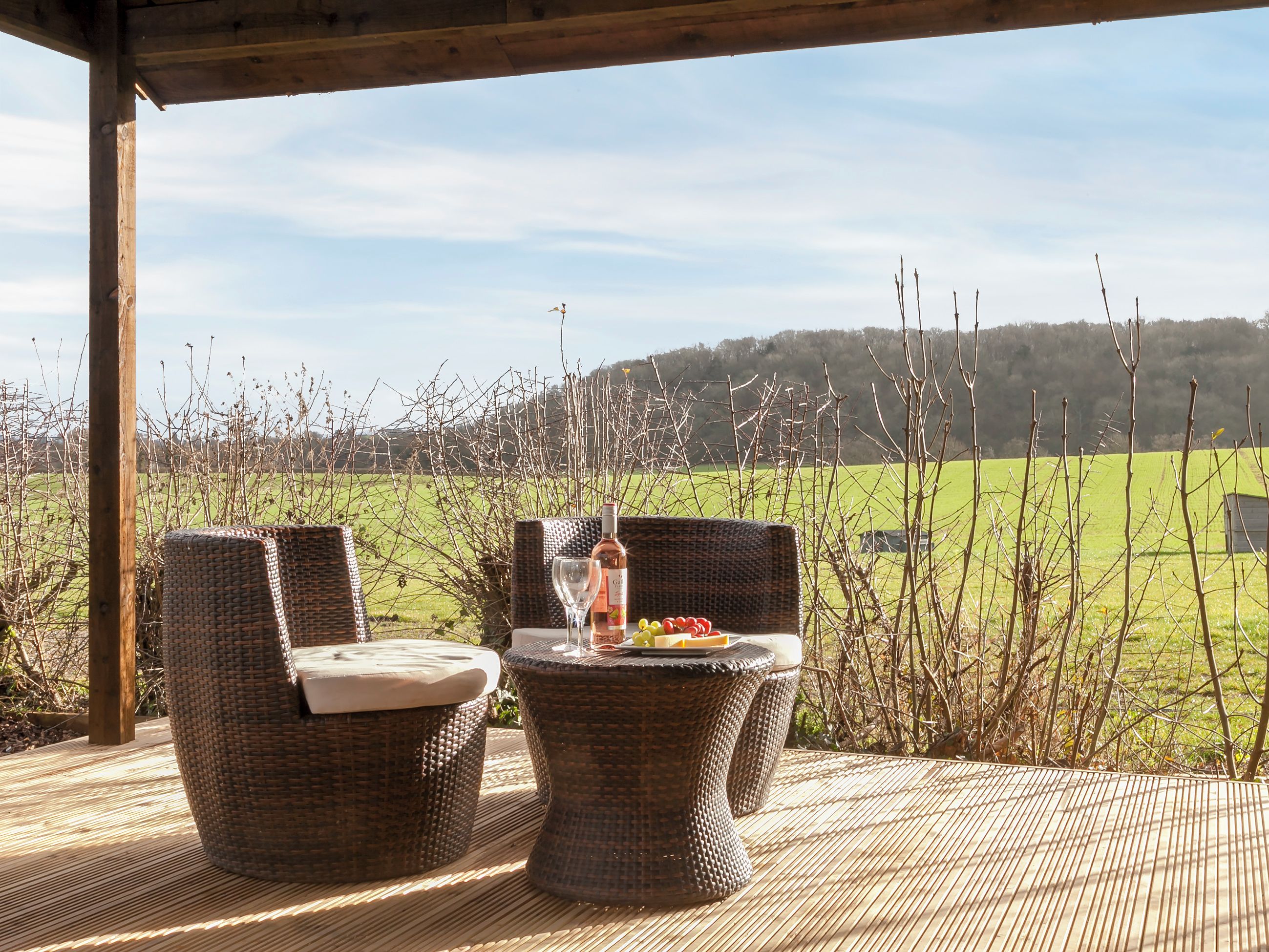 A covered outdoor seating area with wicker furniture and a table set with a bottle and glasses.