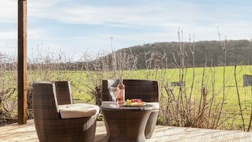 A covered outdoor seating area with wicker furniture and a table set with a bottle and glasses.