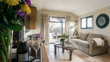 A living room with a sofa, coffee table, and a bottle of wine. There is a window with curtains and a view of the outside.