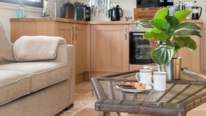 A modern kitchen with wooden cabinets, a dining table with a plant, and a sofa. - 1 bedroom accommodation in Rudford, near Gloucester (Rudford, near Gloucester)