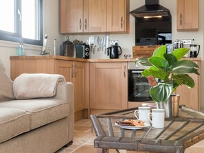A modern kitchen with wooden cabinets, a dining table with a plant, and a sofa. - 1 bedroom accommodation in Rudford, near Gloucester (Rudford, near Gloucester)
