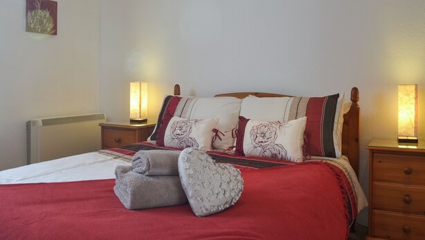 A neatly made bed with a red blanket, multiple pillows, and a bedside lamp. - 1 bedroom accommodation in Lostwithiel (Lostwithiel)