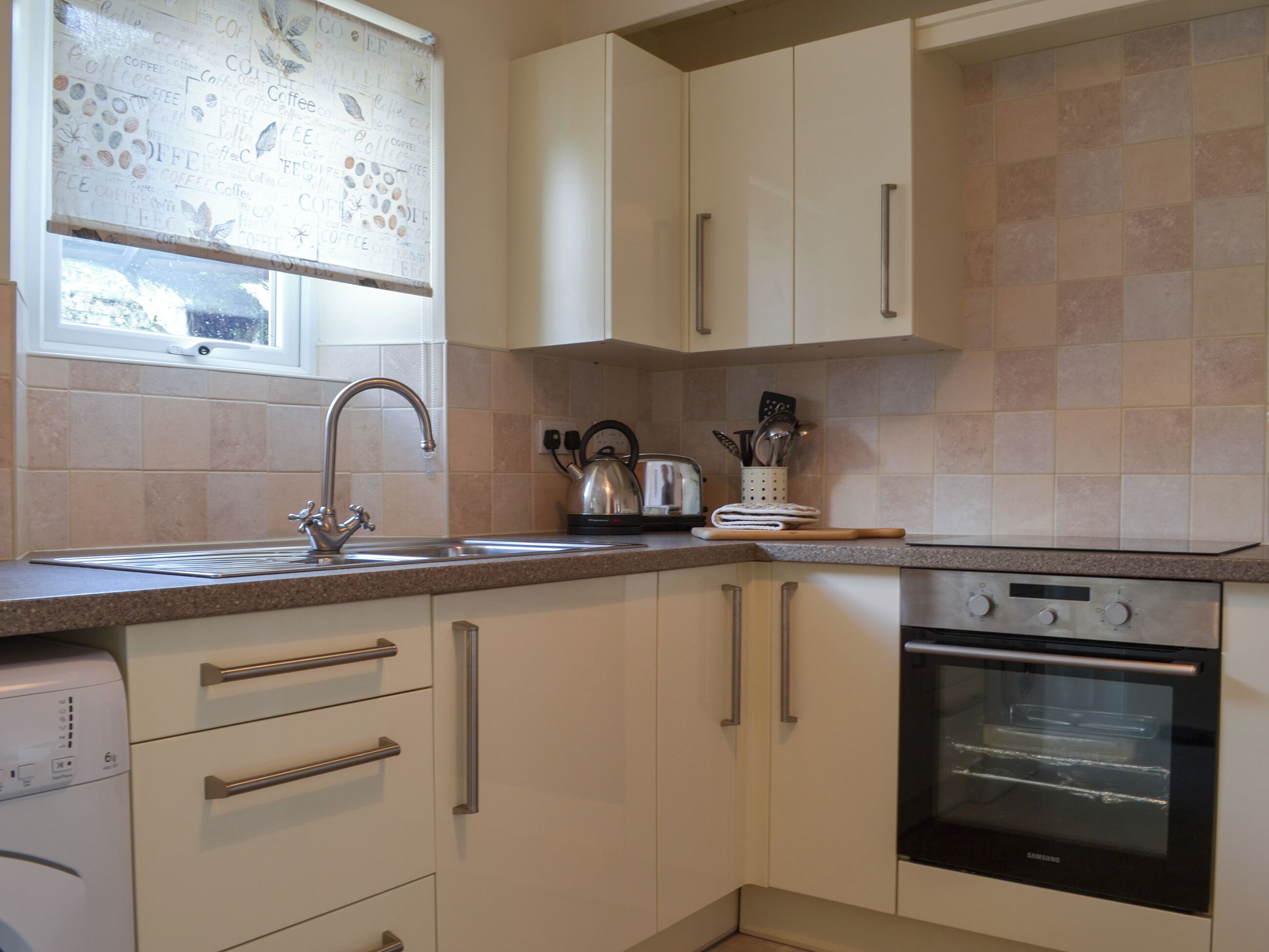 A kitchen with a stainless steel sink, a kettle, a toaster, and a Samsung oven.