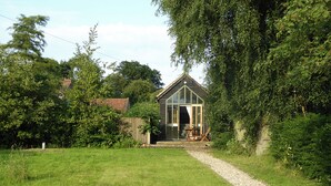 A small, rustic wooden structure with a sloped roof, surrounded by lush greenery and a gravel path leading to it. - 1 bedroom accommodation in Hoe, near Dereham (Hoe, near Dereham)