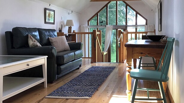A cozy living room with a black leather sofa, a wooden dining table, and a teal chair. - 1 bedroom accommodation in Hoe, near Dereham (Hoe, near Dereham)