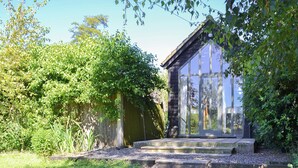 A garden with a stone pathway leading to a wooden building with large windows. - 1 bedroom accommodation in Hoe, near Dereham (Hoe, near Dereham)