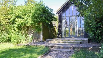A garden with a stone pathway leading to a wooden building with large windows.