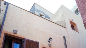 A building with a beige facade, wooden shutters on windows, a central door, and a small outdoor area with steps leading up to the entrance. - Historic house 3 bedrooms 3 bathrooms with panoramic terrace (CASTELSARDO)