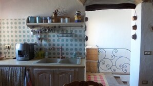 A kitchen with a coffee maker, a sink, and a hanging rack with utensils. There is a stone archway and a patterned wall. - Historic house 3 bedrooms 3 bathrooms with panoramic terrace (CASTELSARDO)