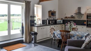 A modern kitchen with a dining area, featuring a large window, a built-in oven, and a view of the outdoors. - Little Barn Tynely Farm (Tynely, near Embleton)