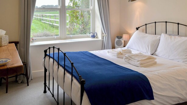 A bedroom with a bed, a bedside table, a lamp, and a window with curtains. - Little Barn Tynely Farm (Tynely, near Embleton)
