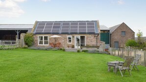 A stone house with a solar panel roof, a covered patio with chairs, and a grassy yard. - Little Barn Tynely Farm (Tynely, near Embleton)
